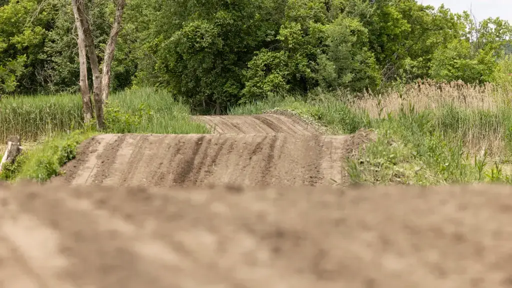 Une piste de motocross en terre battue avec plusieurs sauts et virages serpente à travers une végétation verte et des arbres denses sous un ciel nuageux.