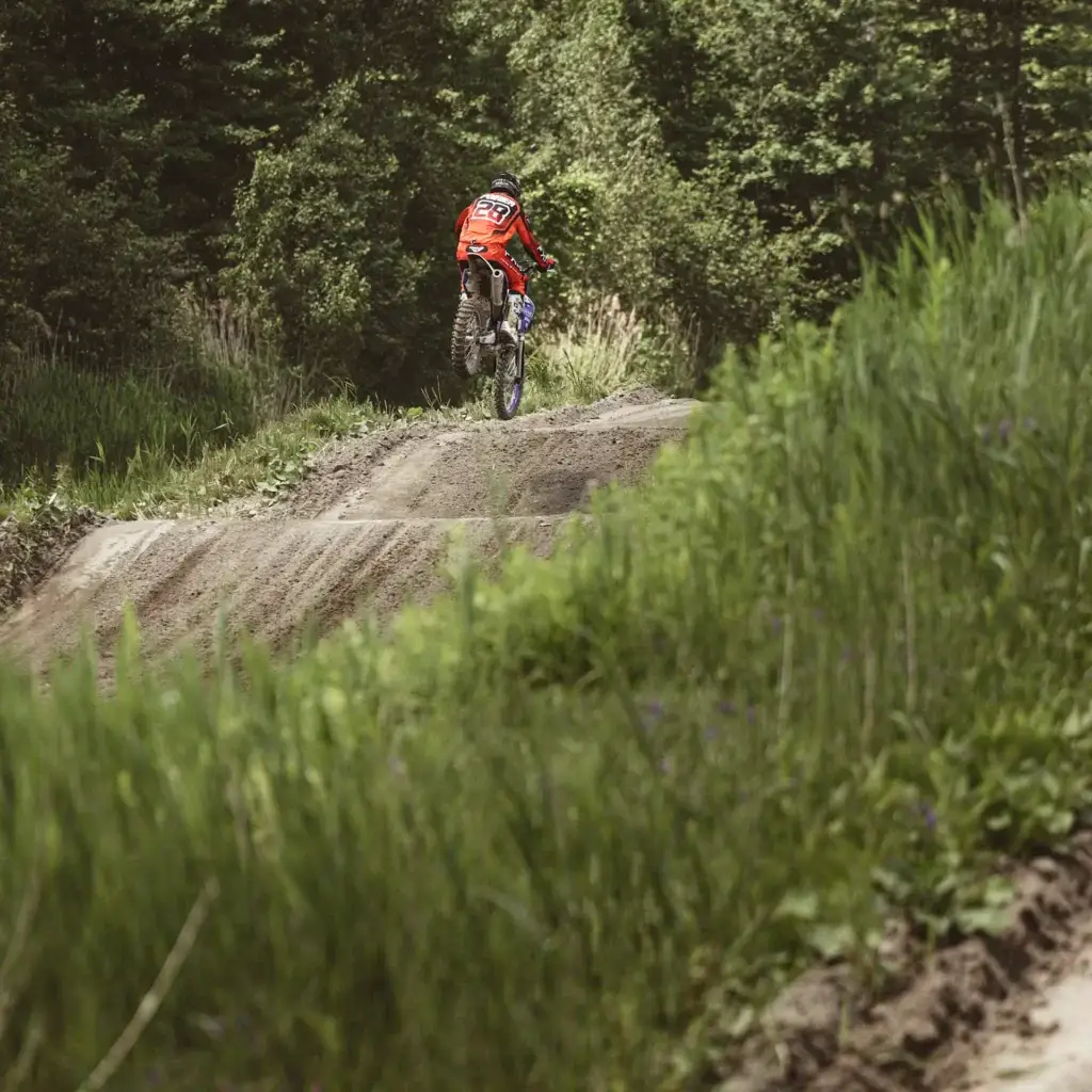 Une personne portant une veste orange roule en VTT sur un chemin de terre dans une forêt verdoyante.