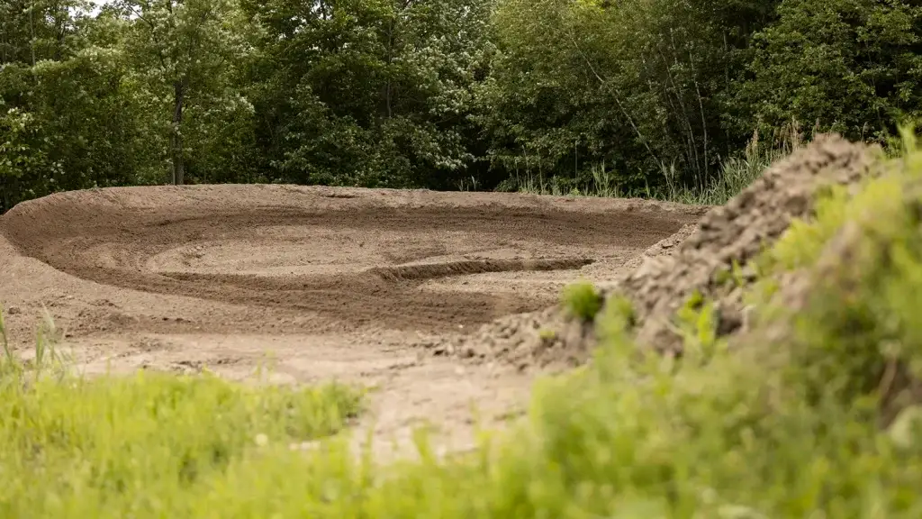 Une piste de motocross avec un virage serré, entourée d'herbe verte et d'arbres denses en arrière-plan, à la lumière du jour.